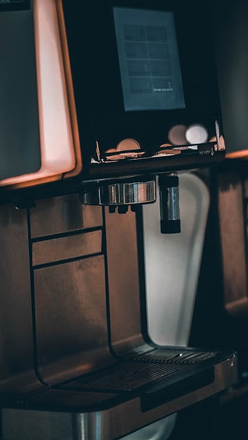 Automatic bean-to-cup machine on a counter, dispensing head lit from the side